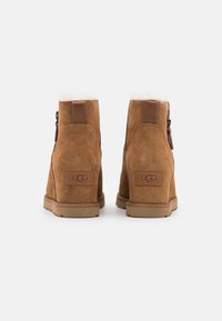Bottines en daim marron avec une doublure en fourrure, dotées d'une fermeture éclair latérale et d'un accent en cuir marron au talon. Logo UGG à l'arrière.