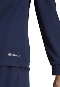 Marineblaue Langarmshirt aus strukturiertem Stoff, mit einem kreisförmigen Logo und dem Schriftzug "AEROREADY" am unteren Saum.