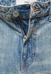Light blue denim jeans featuring a metal button, zipper fly, and orange stitching. The fabric has a faded texture with visible seams.
