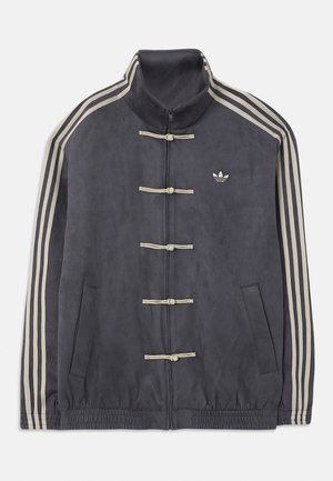 Tmavě šedá sportovní bunda Adidas s béžovými pruhy na rukávech, béžovými stahovacími knoflíky vpředu, dvěma kapsami a malým logem Adidas na hrudi.