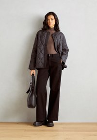 Qulitana črna jakna s krožnim izrezom, rjav prilegajoč top, črne široke hlače in masivne črne platforme. Črna torba z dolgo naramnico.