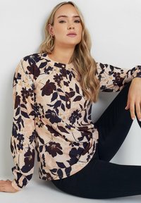 Blusa floreale in pesca chiaro con motivi viola scuro e gialli, scollatura rotonda, patta con un solo bottone e maniche lunghe elasticizzate.