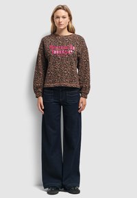 Sweat-shirt à imprimé léopard avec le texte rose "french muse", associé à un jean large noir et des chaussures noires. Tissu doux, coupe décontractée.