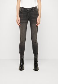 Jeans negros ajustados con un lavado desgastado, cinco bolsillos, cierre con botón de tono plateado y textura suave, combinados con botines negros.