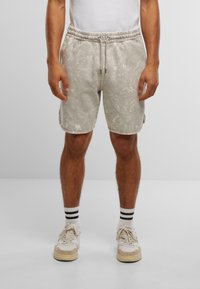 Shorts en tie-dye gris avec une taille élastique et un cordon de serrage. Présente des poches latérales et une coupe décontractée, associés à des baskets blanches et des chaussettes rayées.