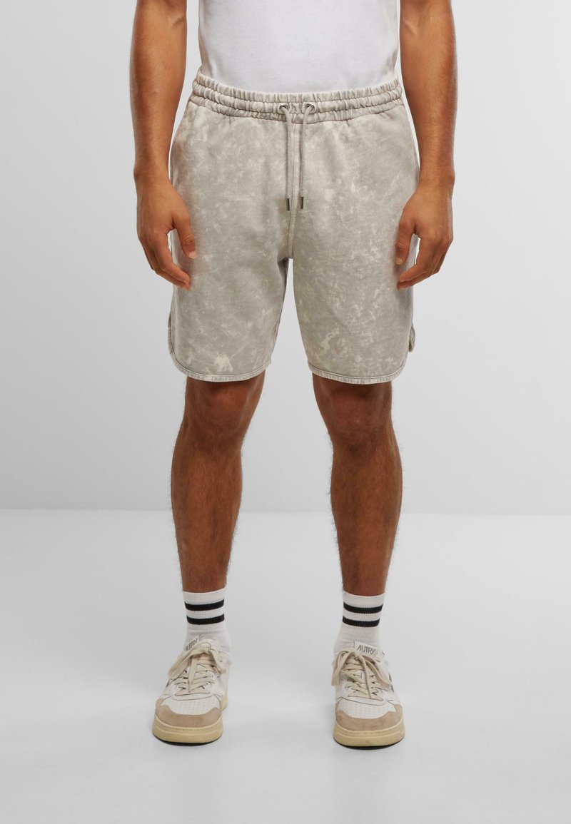 Shorts en tie-dye gris avec une taille élastique et un cordon de serrage. Présente des poches latérales et une coupe décontractée, associés à des baskets blanches et des chaussettes rayées.