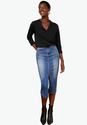 Must eelge pikkade varrukatega pluus, millele on kombineeritud põlve pikkuses helesinine denim pencil seelik, millel on ees lõhik, kantud mustade pahkluuga saapatega.