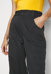 Svarta cargo-byxor med elastisk midja, flera fickor och subtilt varumärkesdetalj. Tillverkade av ett hållbart och lätt material.