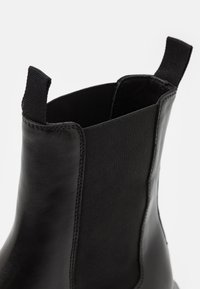 Černé kotníkové boty s hladkým koženým tělem, elastickými bočními panely a texturovaným svrškem pro lepší úchop. Minimalistický design s detaily prošití.