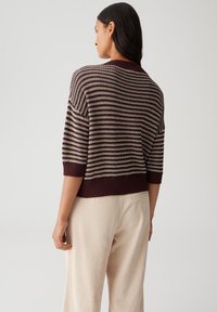 Woman wearing a short-sleeve striped knit sweater in brown and cream, paired with high-waisted beige corduroy pants, shown from behind.