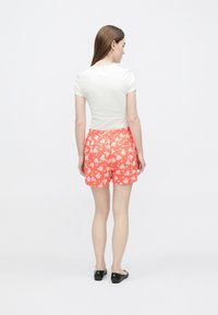 Vit kortärmad topp och korallfärgade shorts med blommönster. Shortsen har resår i midjan och en avslappnad passform, bärs med svarta ballerinaskor.