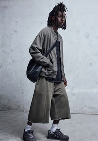 Overdimensioneret olivengrønt sweatshirt over en sort t-shirt, parret med løstsiddende olivengrønne shorts og grå sneakers. Sort crossbody taske, korte sokker.