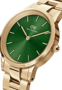 Kuldtooni metallkell rohelise dialsiga, minimaalsete kuldsete tunni näitajatega ja "Daniel Wellington" logo koonusel, näidates kellaaega 10:10.