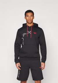 Svart hoodie med röda accenter och framficka; har logotryck och dragsnören. Matcher med svarta shorts.