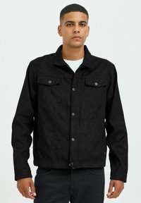 Veste en denim noir avec une finition texturée, comportant un col à pointes, une fermeture à boutons à l'avant, et deux poches sur la poitrine avec rabats.