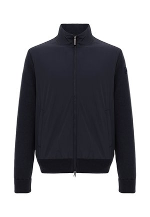Sort jakke med fuld lynlås, ribbet manchetter og kant, opretstående krave, to sidelommer og teksturerede ærmer med et rundt logopatch på venstre ærme.