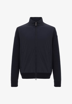 Sort jakke med fuld lynlås, ribbet manchetter og kant, opretstående krave, to sidelommer og teksturerede ærmer med et rundt logopatch på venstre ærme.