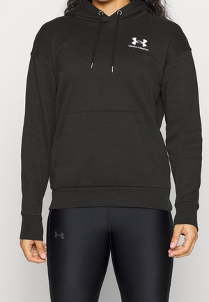 Person iført sort Under Armour hættetrøje med frontlomme og sorte tætsiddende leggings med logo på venstre lår.