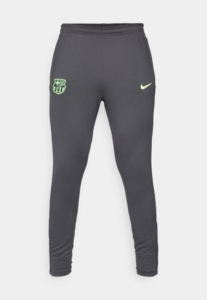 Pantaloni sportivi grigi con un design aderente, caratterizzati da un logo Nike verde lime e un emblema del club Barcellona su coscia sinistra. Tessuto elasticizzato.