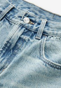 Jeans de mezclilla azul claro con un lavado desgastado, que cuentan con un botón de metal plateado, costuras en contraste y un diseño de cinco bolsillos.