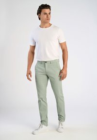 Tenue masculine composée d'un t-shirt blanc ajusté et d'un pantalon tailleur vert clair, associée à des baskets blanches. Design minimaliste et couleurs unies.