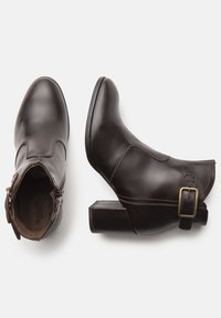 Botas de piel marrón de tobillo con puntera redonda, tacón cuadrado, cremallera lateral y detalle decorativo de hebilla en el lado exterior.