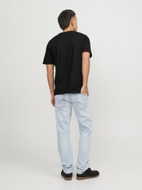 Zwarte T-shirt met korte mouwen, lichtblauwe jeans en zwarte schoenen. De stof lijkt soepel; het T-shirt heeft een klassiek crew neck ontwerp.