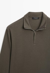Dunkelgrüner Pullover mit einem Viertel-Reißverschluss-Kragen und strukturiertem Stoff. Hat ein minimalistisches Design und dezente Nähdetails.