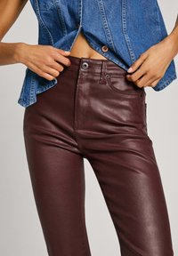 Burgundy leather pants with a glossy finish, five-pocket design, and belt loops; paired with a denim sleeveless top, showing a midriff.