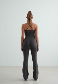 Fekete, testhezálló sportöltözet, amely halter felsőből áll vékony pántokkal és bővülő, magas derekú leggingsből. Simás textúra és minimalista dizájn jellemzi.