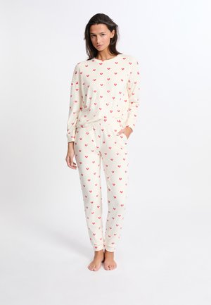 Completo pigiama crema composto da una maglietta a maniche lunghe e pantaloni, decorato con piccoli motivi a cuore rossi, realizzato in tessuto morbido e con una vestibilità comoda.