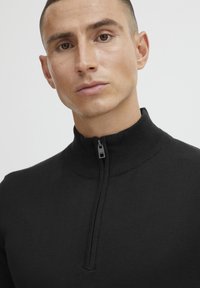 Black zip-up sweater with a high ribbed collar, featuring a smooth texture and a short zipper detail at the front.