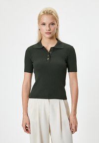 Polo shirt côtelé vert foncé à manches courtes, avec patte de boutonnage et col classique. Texture lisse avec une coupe ajustée.