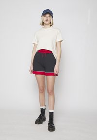Camiseta de algodón blanca, pantalones cortos negros con cintura elástica roja y ribete blanco, combinados con botas negras con cordones y una gorra de denim.