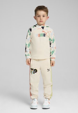 Chándal de niño que presenta una sudadera beige con estampados de animales coloridos y un logo, acompañada de pantalones de chándal beige con acentos laterales y parches.