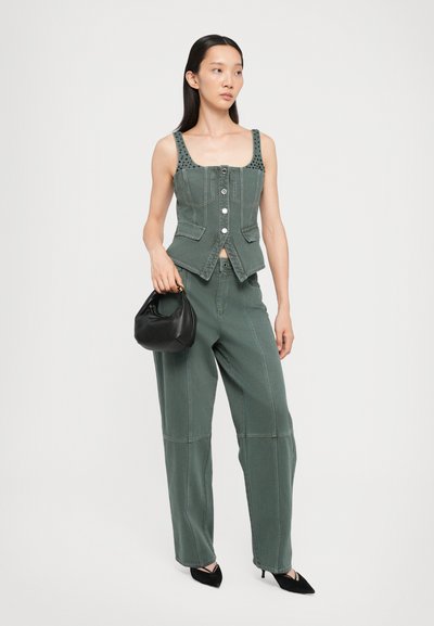 Grüner Denim-Cropped-Top mit Knopfleiste und gepolsterten Trägern, kombiniert mit lockeren grünen Hosen und einer kleinen schwarzen Handtasche. Schwarze High Heel-Schuhe.