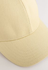 Yellow fabric cap with a textured surface, curved brim, and visible stitching details. The design features a structured crown.