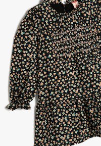 Svart klänning med blommönster i rosa, gult och blått, med smockdetaljer och elastiska manschetter. Utsvängd nederkant.