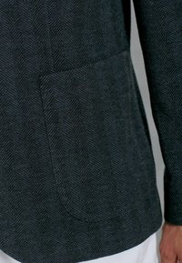 Tissu de blazer à chevrons foncé avec un motif texturé. Comprend une poche cousue sur le côté gauche et une coupe droite à l'ourlet.