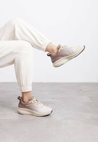 Zapatillas ligeras en tonos beige y malva, con un upper de malla texturizada, cuello acolchado y suela de goma en contraste con un diseño minimalista.