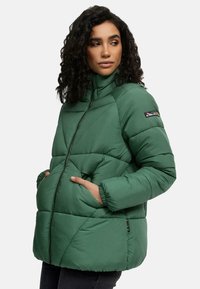 Groene pufferjack met hoge kraag, ritssluiting, voorzakken en elastische manchetten. Beschikt over driehoekige stikpatronen en een logopatch.