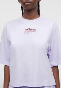 Γυναίκα που φοράει ένα ανοιχτό μωβ oversized T-shirt New Balance Athletics με κοντά μανίκια και στρογγυλή λαιμόκοψη.