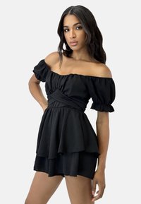 Abito nero scollato sulle spalle con maniche a sbuffo, vita arricciata e gonna a strati. Tessuto morbido con una texture fluida e design senza cuciture.