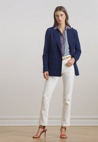 Blazer navy a doppio petto a righe sopra una camicia a righe blu e rosa, abbinato a pantaloni bianchi a gamba dritta e tacchi rossi e beige.