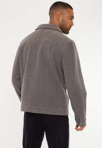 Grå uld-blandingsjakke med notch-krave, cropped design og sidelommer. Glat tekstur med subtile syninger.