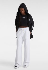 Sort zip-up hoodie med hætte og hvidt logo, parret med løstsiddende lysegrå sweatpants med snøre i livet.