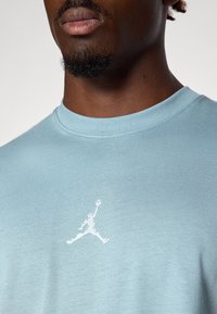Gaiši zils kokvilnas T-krekls ar apaļu kaklu un balto Jumpman logo izšuvumu uz krūtīm. Gluda tekstūra, brīvuma piegriezums.