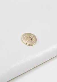 Zbliżenie na złoty metalowy zatrzask na gładkim białym skórzanym materiale.