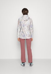 Veste à capuche avec impression florale dans des couleurs pastel, associée à un pantalon rose et des chaussures de sport bleu clair, vue de dos.