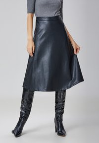 Jupe en cuir noir en forme de A avec une texture lisse, taille haute et longueur genou, associée à des bottes high-tech brillantes à motif crocodile.